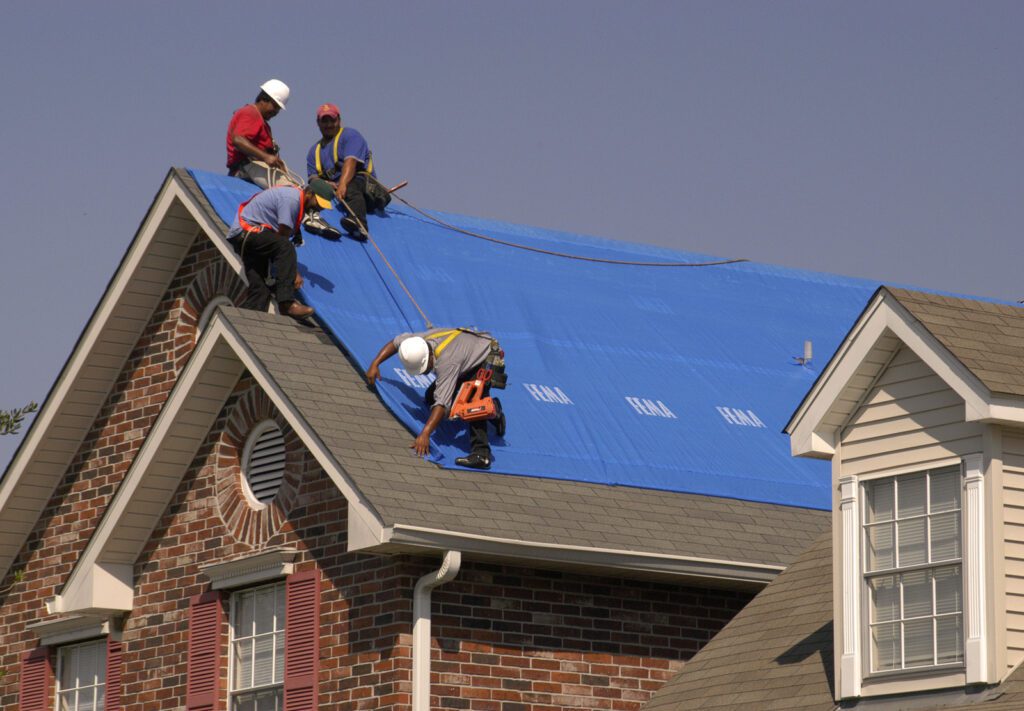roof with blue tarp and three workers