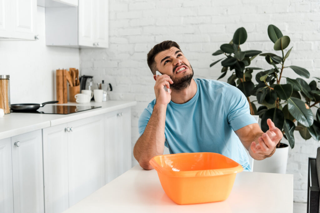 man looking at leaking roof while talking on phone