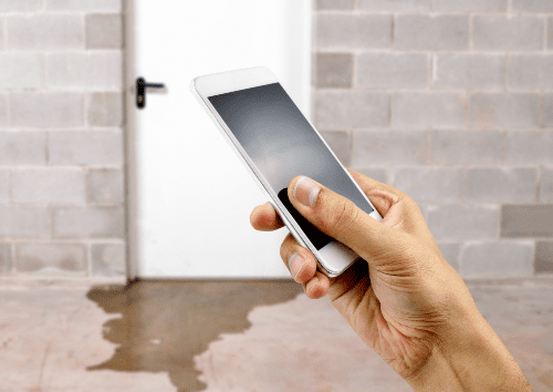 Man holding smartphone in front of water leaking under door