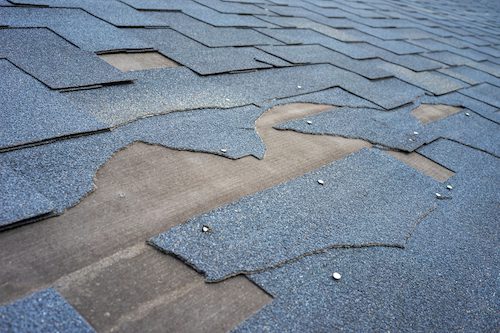 Сlose up view of bitumen shingles roof damage that needs repair.